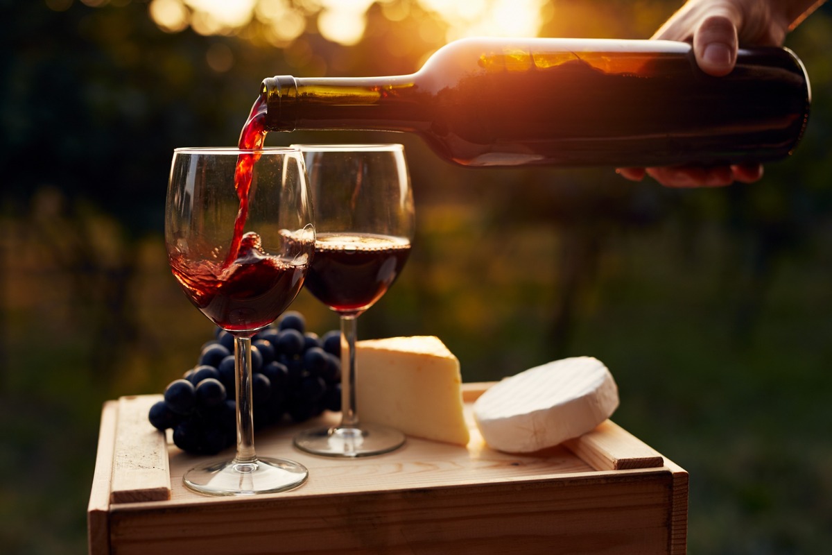 Botella de vino sirviendo en dos copas con desgutación de quesos